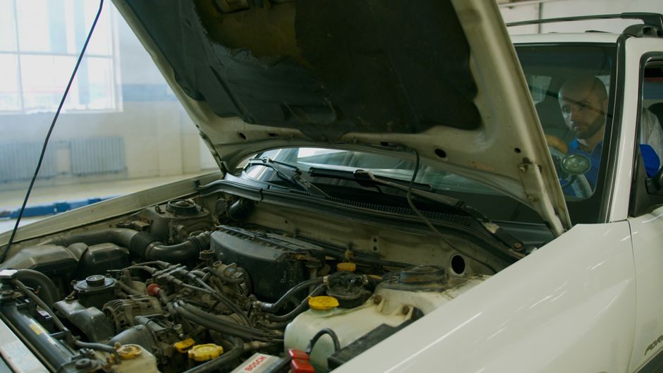 Conducteur qui écoute le bruit d'un moteur capot ouvert dans un garage